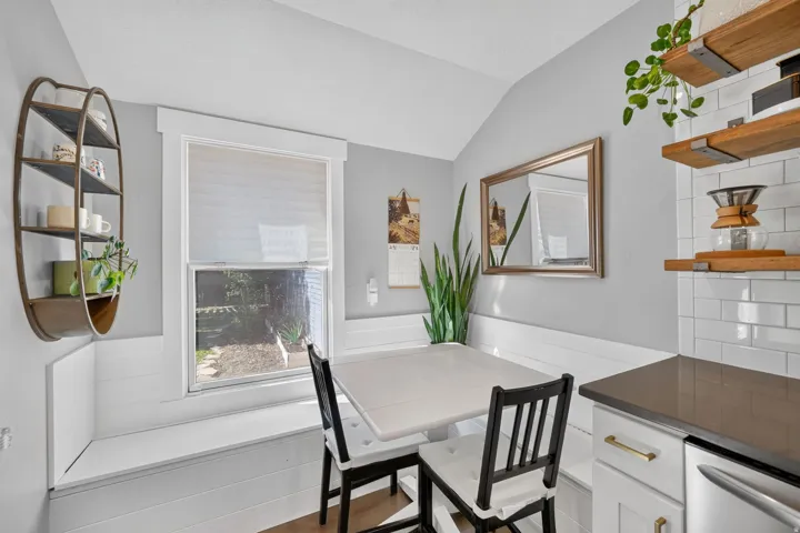 Built-in banquet seating, white subway tile backsplash, open wood shelving, stainless steel appliance, and gold-finish cabinet hardware