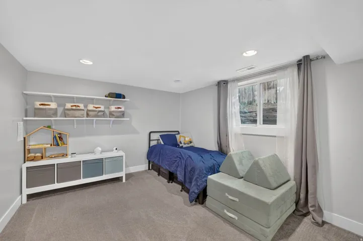 Recessed lighting, wall-mounted shelving, built-in storage unit, carpeted flooring, and a single window with white trim