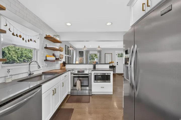 Kitchen featuring white shaker cabinetry, stainless steel appliances, dark countertops, a subway tile backsplash, and wood-finish flooring