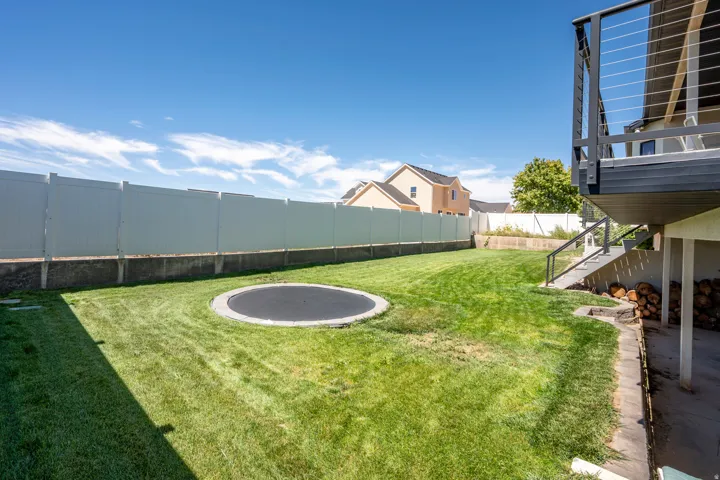 Expansive lawn with a built-in trampoline, complemented by a white privacy fence and a composite deck with cable railing