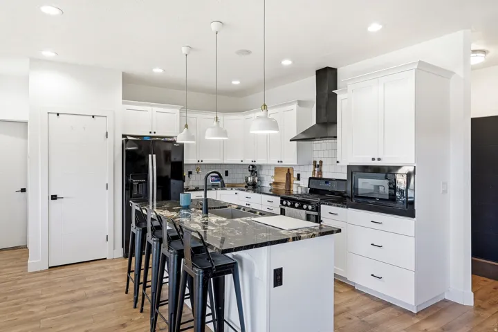 Kitchen featuring white shaker cabinetry, dark countertops, a large island with sink, black stainless steel appliances, and wood-finish flooring