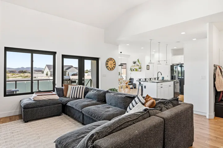 Vaulted ceiling, black-framed windows, glass patio door, white shaker kitchen cabinetry, and wood-finish flooring