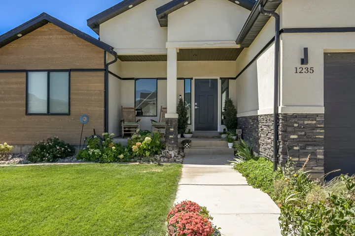 Stucco and stacked stone exterior, covered entry, concrete walkway, and landscaped garden beds