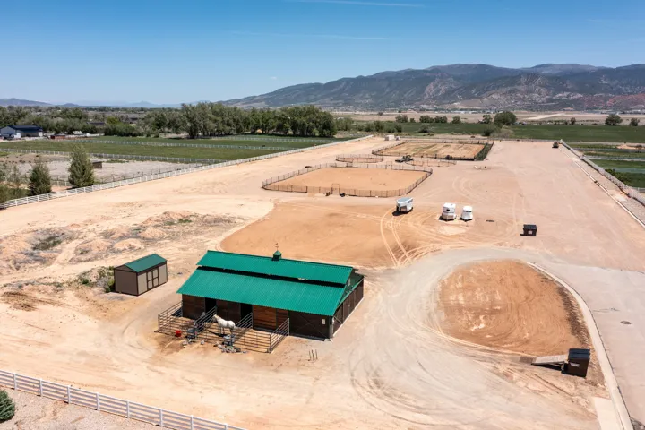 Barn structure with green roofing, multiple fenced enclosures, and a surrounding expansive dirt lot