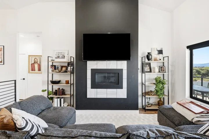 Vaulted ceiling, contemporary fireplace with tile surround, built-in shelving, and large window with outdoor scenery