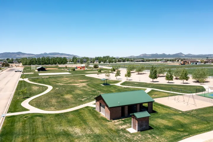 Expansive park area featuring paved walking paths, multiple green spaces, mature trees, and mountain scenery in the background