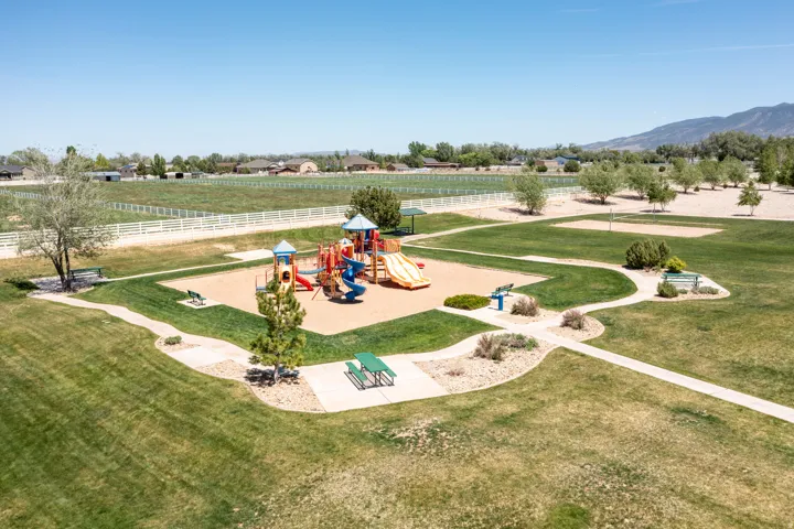 Expansive park area featuring a colorful playground, paved pathways, green picnic tables, and mature trees