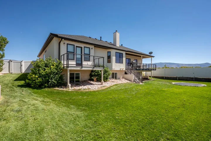Expansive rear yard with a manicured lawn, full privacy fencing, and an upper-level deck with metal railings