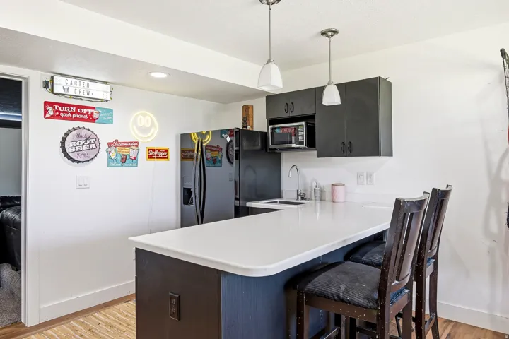 Kitchenette featuring dark cabinetry, a countertop with integrated sink, two pendant lights, and wood-finish flooring