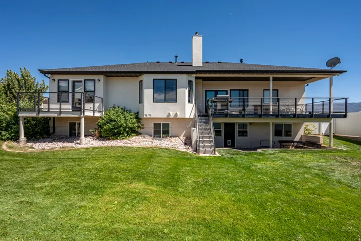 Expansive rear yard featuring a manicured lawn, two elevated decks with dark railings, and a covered patio area