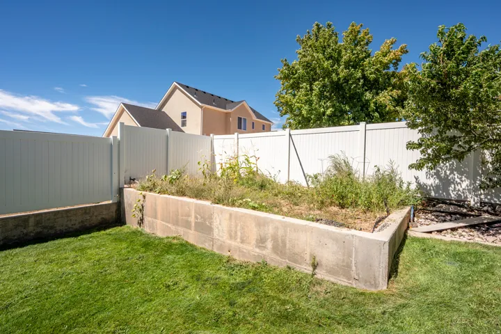 Manicured lawn with a concrete retaining wall, white privacy fencing, and mature trees
