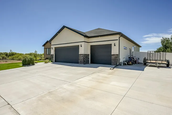Two-car garage with dark gray doors and exterior lighting, featuring a light stucco facade and dark stone accents