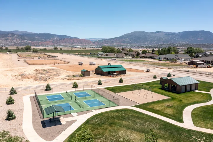 Four pickleball courts with perimeter fencing, a covered seating area, and a paved pathway