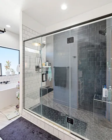 Glass-enclosed shower with dark subway tile, geometric tile shower floor, and built-in shower bench