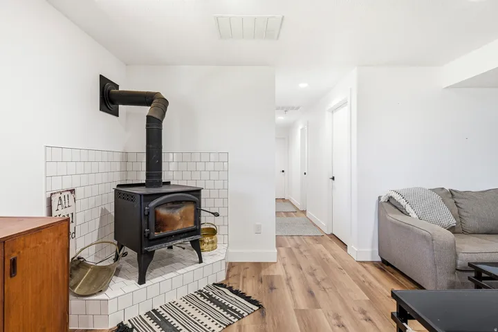 Wood-finish flooring throughout, white walls, and a wood-burning stove with white subway tile surround