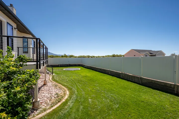 Expansive backyard featuring a manicured lawn, white privacy fence, and a raised deck with black railings
