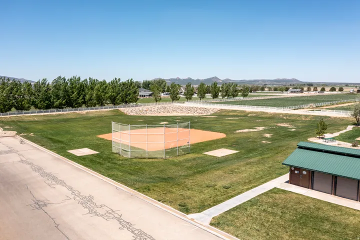 Baseball diamond with a fenced backstop, surrounded by a grassy field and a paved pathway