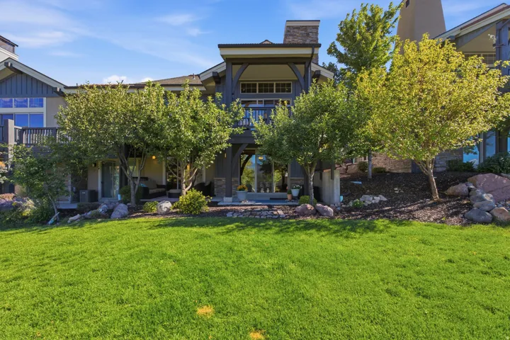 Expansive green lawn, multi-level dwelling with stone accents, covered outdoor patio, and mature trees