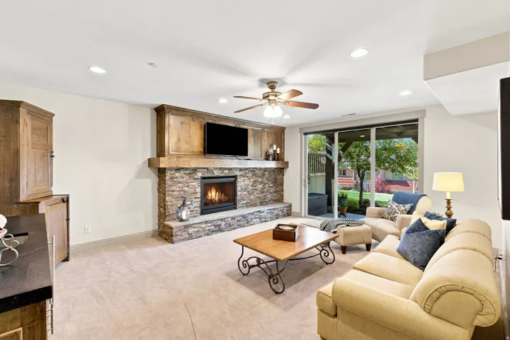 Built-in stone fireplace with wood mantle, sliding glass patio door, recessed lighting, ceiling fan, and built-in wood cabinetry