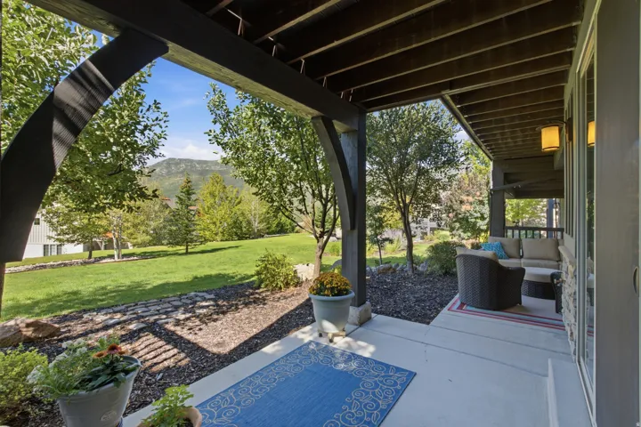 Covered patio with concrete flooring, stone veneer exterior, recessed lighting, and expansive backyard with a mountain backdrop