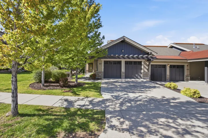 Exterior featuring a multi-car garage, stone and siding accents, and a front yard with mature trees