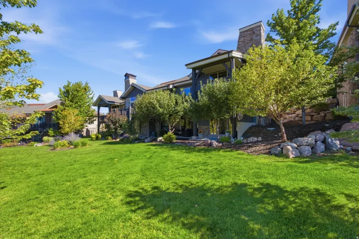 Expansive green lawn with mature trees and landscaped rock retaining walls, complementing the property's exterior