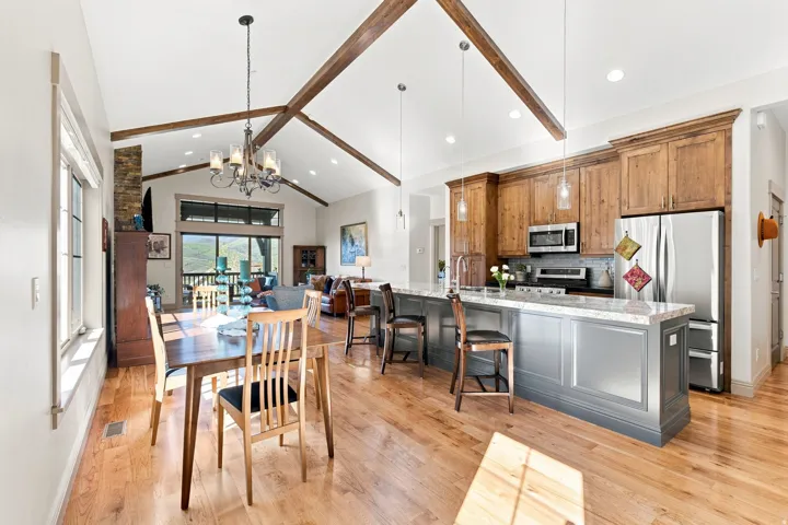 Vaulted ceilings with exposed wood beams, wood-finish flooring, island kitchen with integrated seating, stainless steel appliances, and stone countertops
