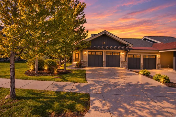 Stone and siding exterior with multiple garage bays, an architectural shingle roof, and a mature landscaped yard with established trees