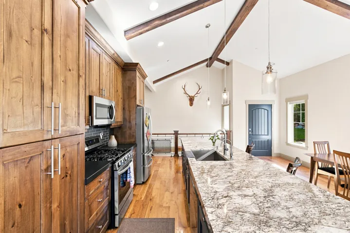 Kitchen featuring wood cabinetry, stainless steel appliances, a large island with a stone countertop, and vaulted ceilings with exposed beams