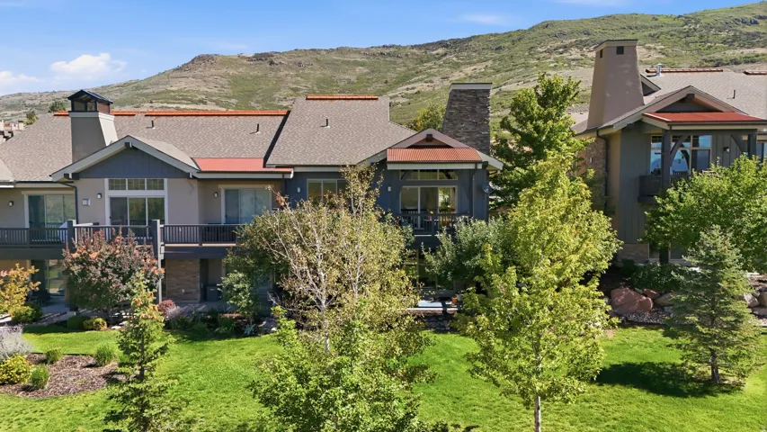 Multi-level residence featuring balconies, a prominent stone chimney, and a landscaped backyard with mature trees