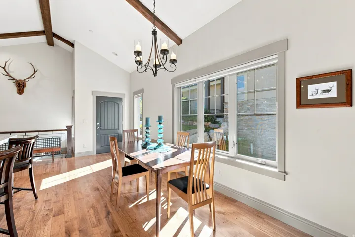 Vaulted ceiling with wood beams, wood-finish flooring, large window with trim, dark paneled door, and an ornate chandelier
