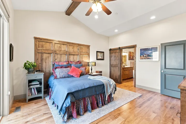 Vaulted ceiling with wood-finish beam and ceiling fan, wood-finish flooring, and a large wood headboard
