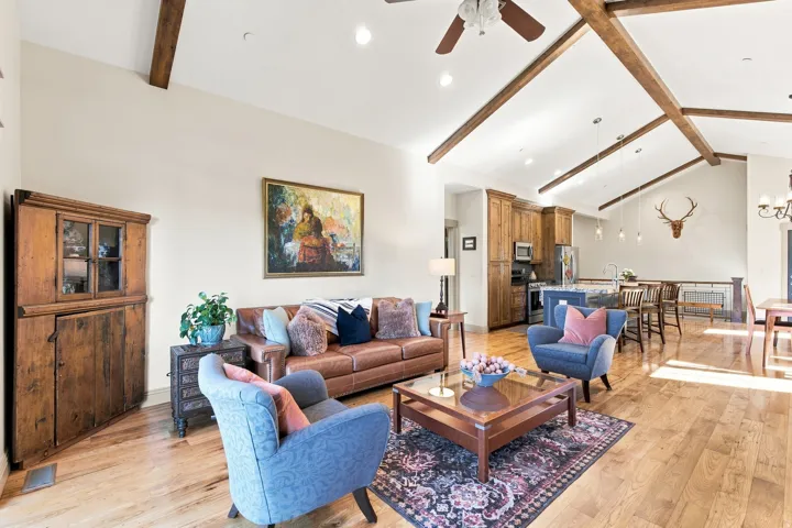 Vaulted ceiling with exposed wood beams, wood-finish flooring throughout, recessed lighting, built-in wooden cabinetry, and stainless steel appliances