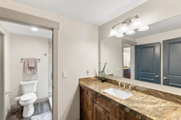 Dual-sink vanity with a granite countertop, wood-finish cabinetry, and a large wall-mounted mirror