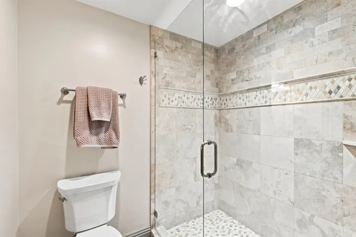 Glass-enclosed shower featuring large format wall tiles, decorative accent banding, and a mosaic tile floor