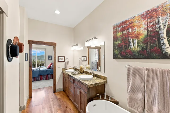 Dual sink vanity with stone countertop, hardwood flooring, recessed lighting, and a freestanding soaking tub