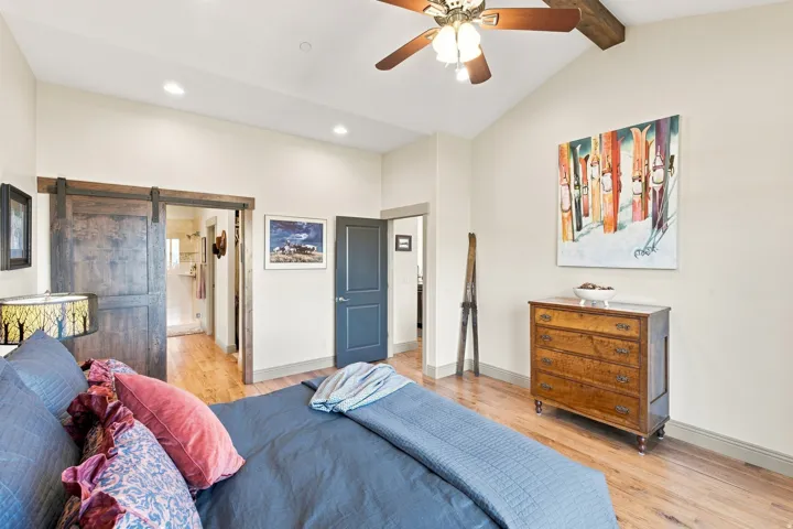 Vaulted ceiling with wood beam accents, wood-finish flooring, recessed lighting, and a dark wood barn door