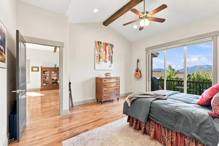 Vaulted ceiling with exposed wood beam, wood-finish flooring, sliding glass door to exterior balcony, recessed lighting, and ceiling fan
