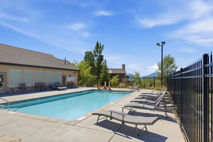 Rectangular swimming pool with a concrete surround, black metal fencing, and a surrounding building with multiple windows