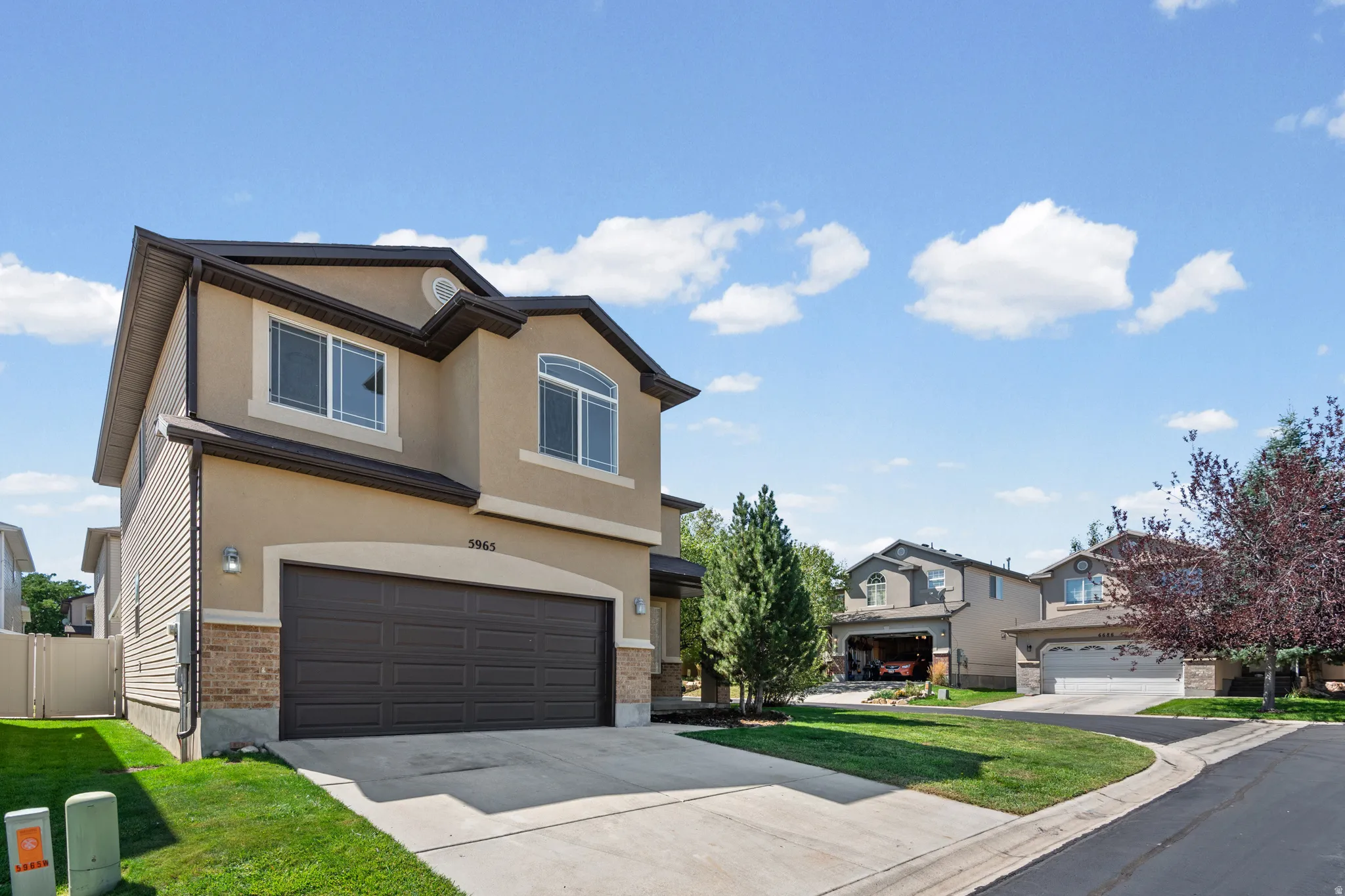 Two-story residence featuring a stucco exterior, an integrated two-car garage, brick accents, a gabled roofline, and a concrete driveway