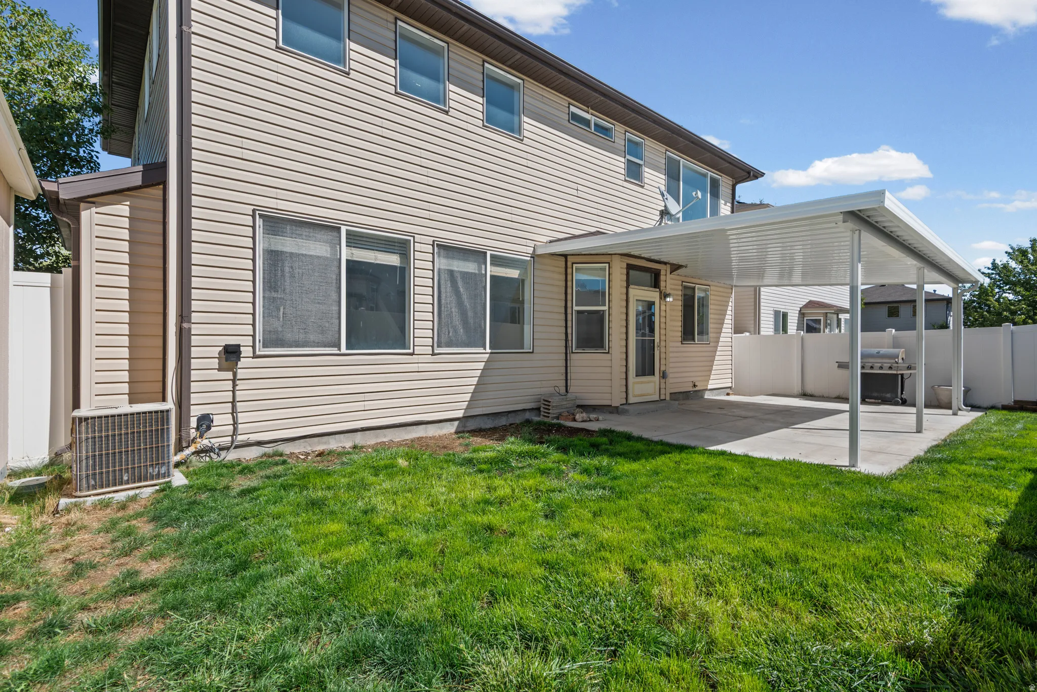 Expansive backyard featuring a covered patio, concrete hardscaping, and a white privacy fence
