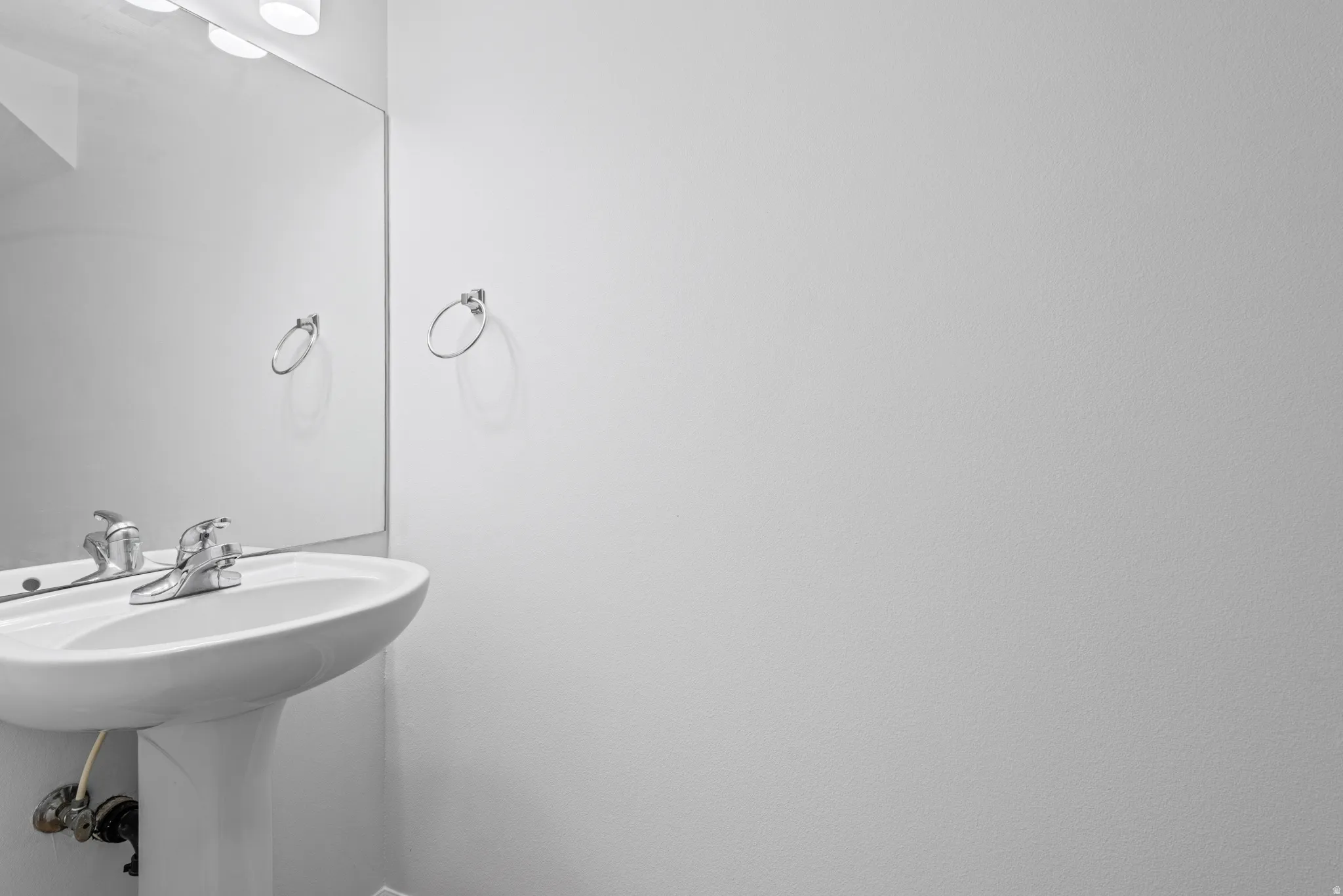 Pedestal sink with chrome faucet, wall-mounted mirror, and overhead lighting