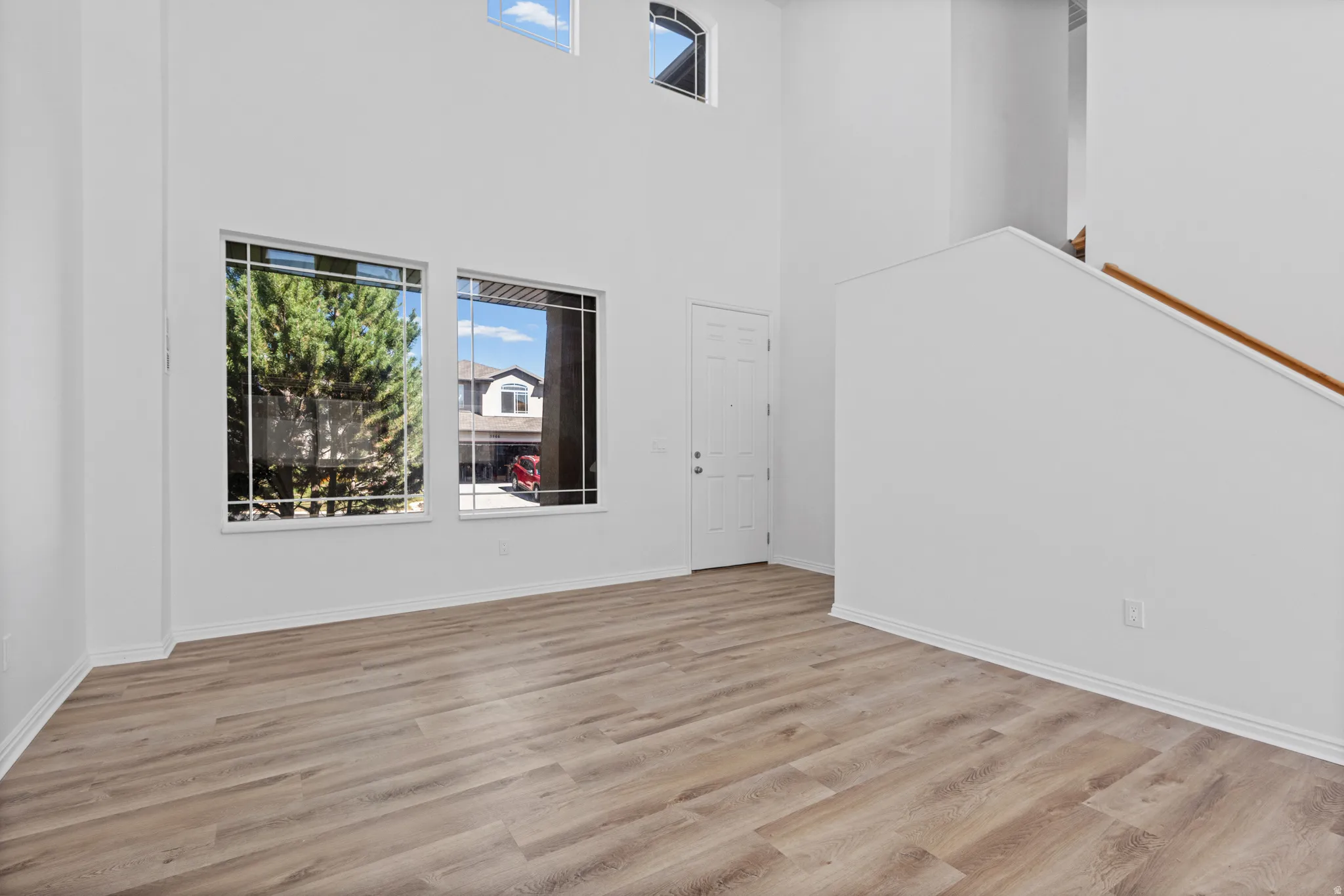 Double-height ceiling, arched window, wood-finish flooring, white paneled door, wood handrail