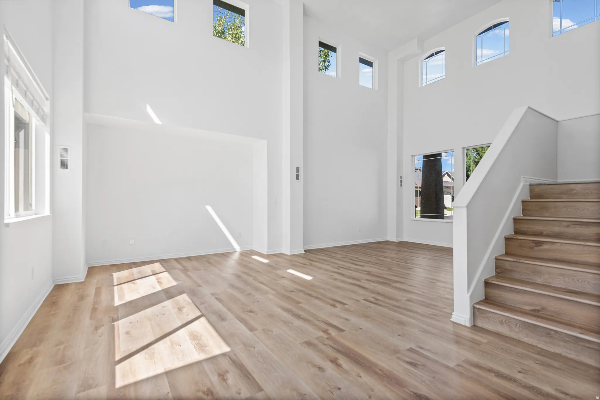 Double-height ceiling, multiple windows, wood-finish flooring, staircase with wood treads, white walls