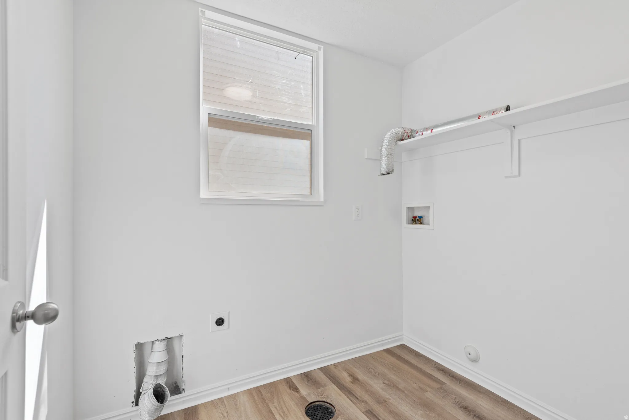 Laundry room featuring wood-finish flooring, a window with a white frame, and a built-in white shelf