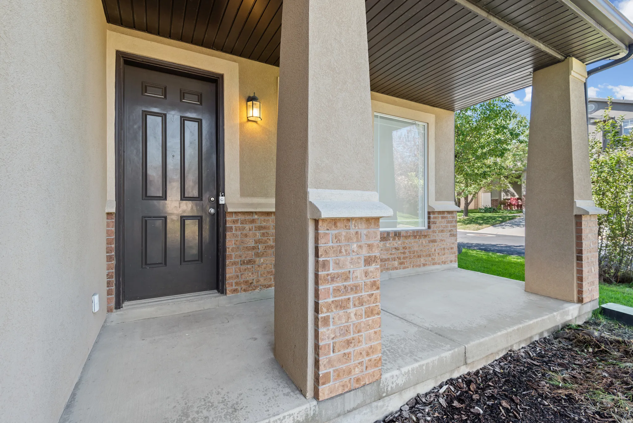 Covered front porch featuring a dark paneled entry door, exterior sconce lighting, and brick accents