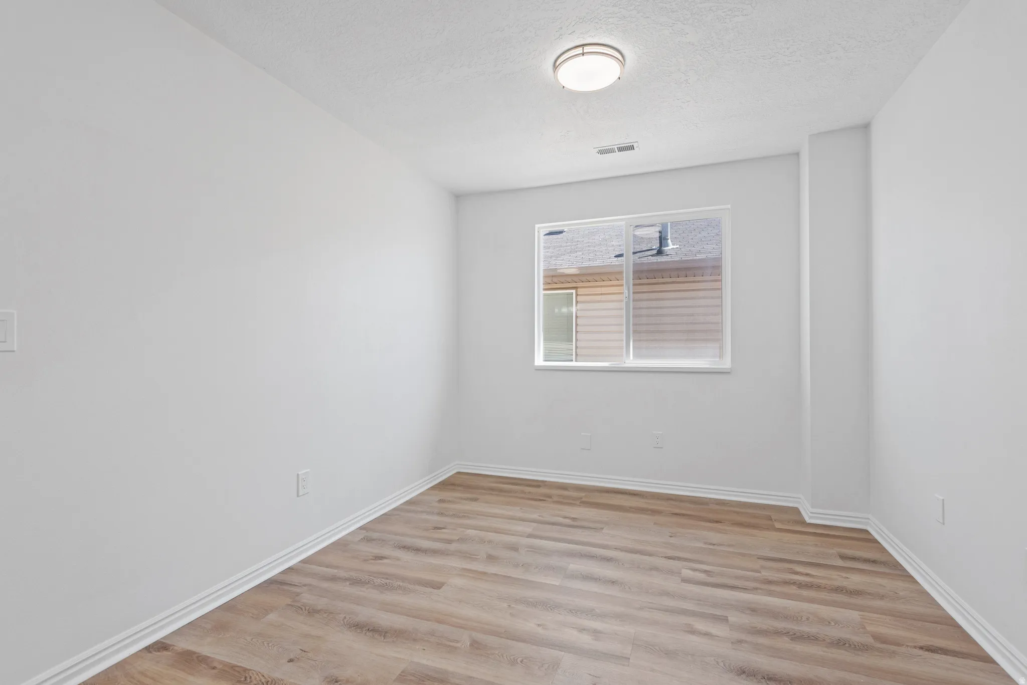 Recessed ceiling light fixture, wood-finish flooring, white trim, and a window with white casing