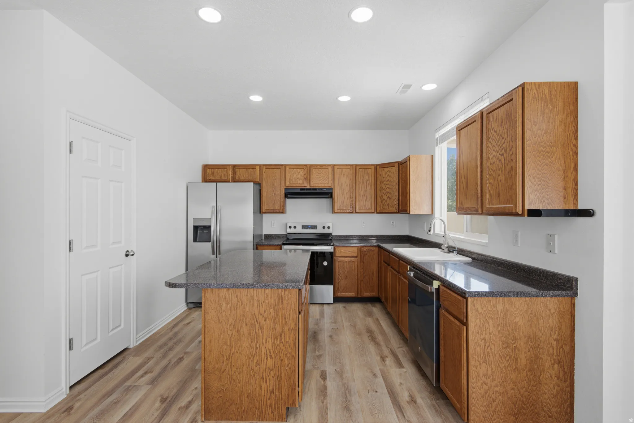 Wood-finish flooring, recessed lighting, wood cabinetry, stainless steel appliances, and a kitchen island with seating