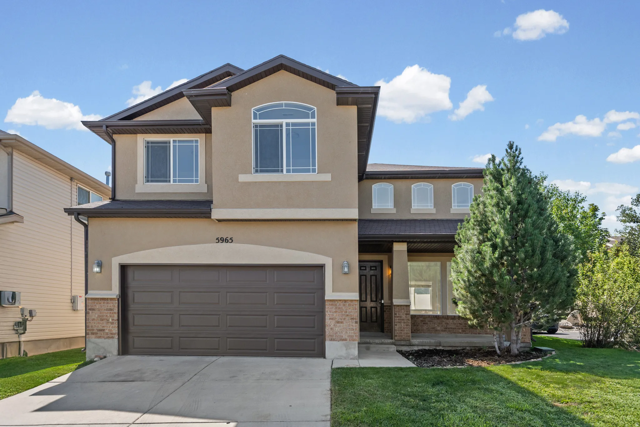 Two-story stucco facade featuring an arched window, a covered front porch, and an attached two-car garage