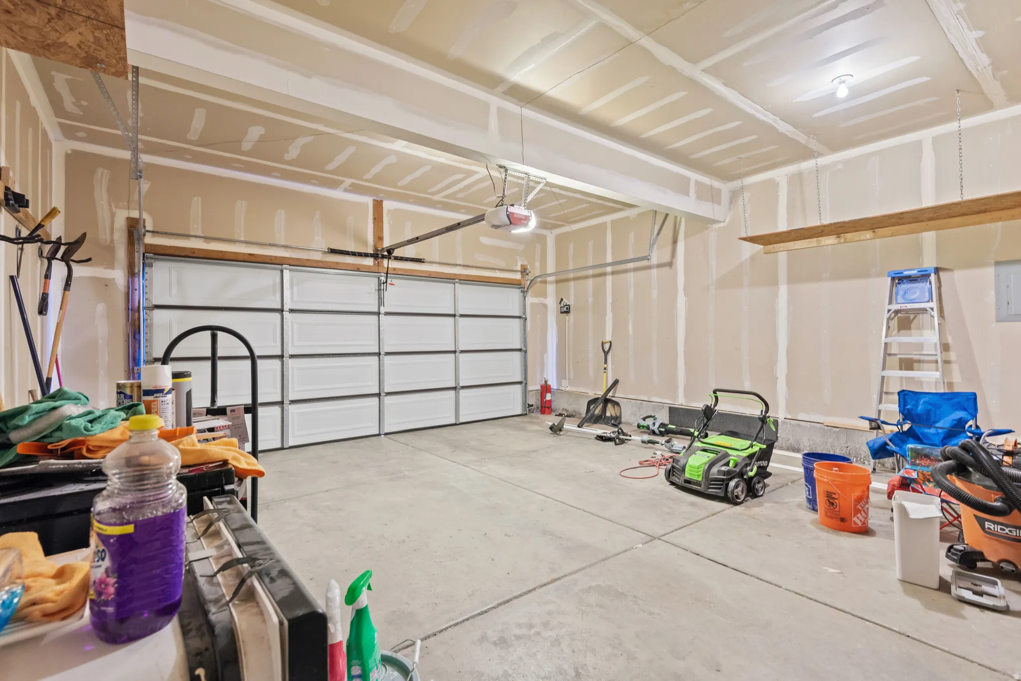 Concrete flooring, overhead lighting, automatic garage door, exposed ceiling joists, drywall ready for finishing